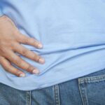 A person in a blue shirt and jeans clutching their hip, possibly indicating pain.