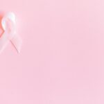 A pink ribbon on a soft pink background symbolizing breast cancer awareness and solidarity.