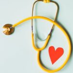 Yellow stethoscope arranged with a red heart cutout on a light green background, symbolizing heart health.