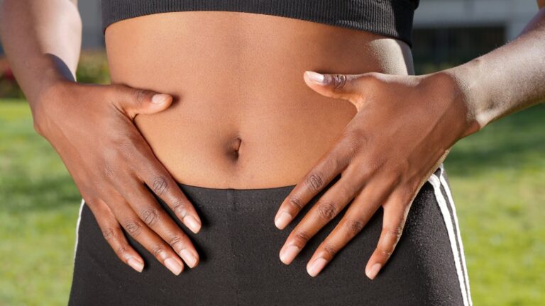 Close-up of a person placing hands on stomach outdoors, emphasizing wellness, skin health, and outdoor exercise.