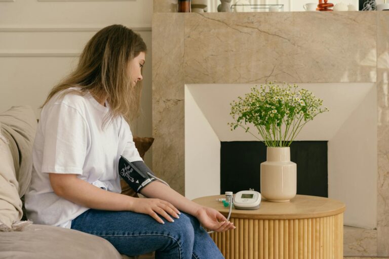 Caucasian woman checking blood pressure with a sphygmomanometer by a vase of flowers indoors.
