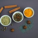 Flat lay of assorted spices including cinnamon, turmeric, and star anise on a dark surface.