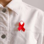 Red ribbon for HIV/AIDS awareness pinned on a white shirt symbolizing support and solidarity.
