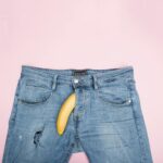 A creative still life featuring blue jeans and a banana against a pink backdrop.
