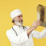 Elderly doctor in white coat examining a chest X-ray image against a bright yellow backdrop.