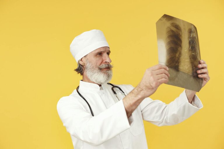 Elderly doctor in white coat examining a chest X-ray image against a bright yellow backdrop.