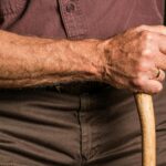 Close-up of a senior adult's hand gripping a wooden walking cane outdoors, symbolizing support and aging.