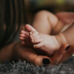 Close-up of a mother's hand gently holding her baby's tiny feet, symbolizing warmth and affection.