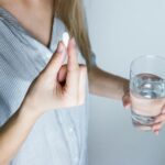 Close-up of a woman holding a pill and a glass of water, ready to take medication.