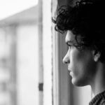 Profile portrait of a young man looking thoughtfully out of a window, in black and white.