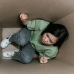 A woman feeling trapped and anxious inside a small cardboard box, symbolizing claustrophobia.