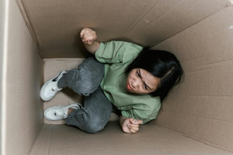 A woman feeling trapped and anxious inside a small cardboard box, symbolizing claustrophobia.