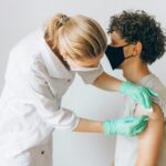 A healthcare worker gives a vaccine shot to a patient wearing a mask, highlighting medical safety and health precautions.