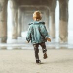 walking boy wearing blue denim jacket under the bridge