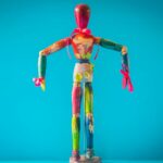 A vibrant wooden mannequin painted in various colors stands out against a blue backdrop.