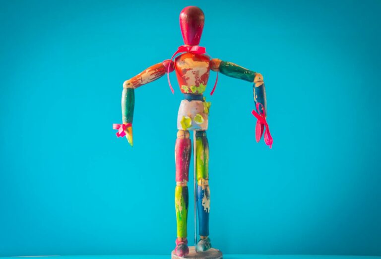 A vibrant wooden mannequin painted in various colors stands out against a blue backdrop.
