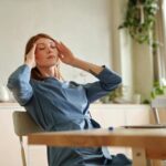 Woman experiencing stress at work, sitting at desk with a laptop, indoors.