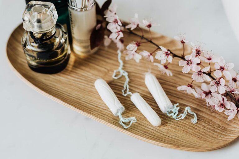 Flat lay of feminine hygiene products, perfumes, and cherry blossoms on a wooden tray.