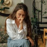 Woman in a white shirt sitting thoughtfully on a vintage sofa indoors.