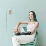 Portrait of a woman with prosthetic arm seated in a stylish interior, wearing a white tank top.