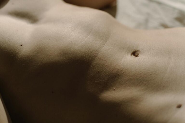 Detailed close-up of human skin featuring belly button, texture, and moles under natural light.