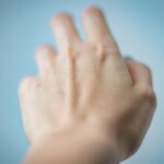 Artistic depiction of a blurred hand reaching against a blue background.