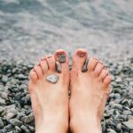 Close-up of female feet with stones on pebbled beach by the water, evoking relaxation and tranquility.