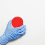 Close-up of a gloved hand holding a petri dish with red liquid, symbolizing laboratory research.