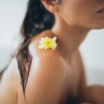 Close-up of a woman relaxing in a bath with a yellow flower on her shoulder.