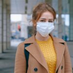 Young woman in a coat and mask stands outdoors, promoting health and safety measures.