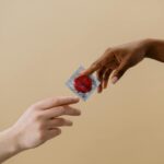 A close-up of two diverse hands exchanging a red condom, promoting safe sex and contraception.