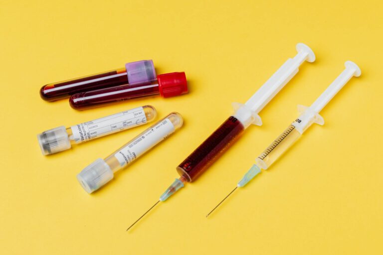 Thalassämie From above of medical syringe with medication near injector with blood sample arranged with filled clinical test tubes placed on yellow background