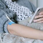 A woman receiving intravenous therapy for cancer treatment while using her phone, symbolizing connection and hope.