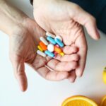 Close-up of hands holding multicolored pills with oranges, symbolizing health and nutrition.