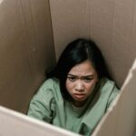 A woman inside a cardboard box symbolizes feelings of anxiety and claustrophobia.