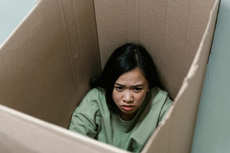 A woman inside a cardboard box symbolizes feelings of anxiety and claustrophobia.